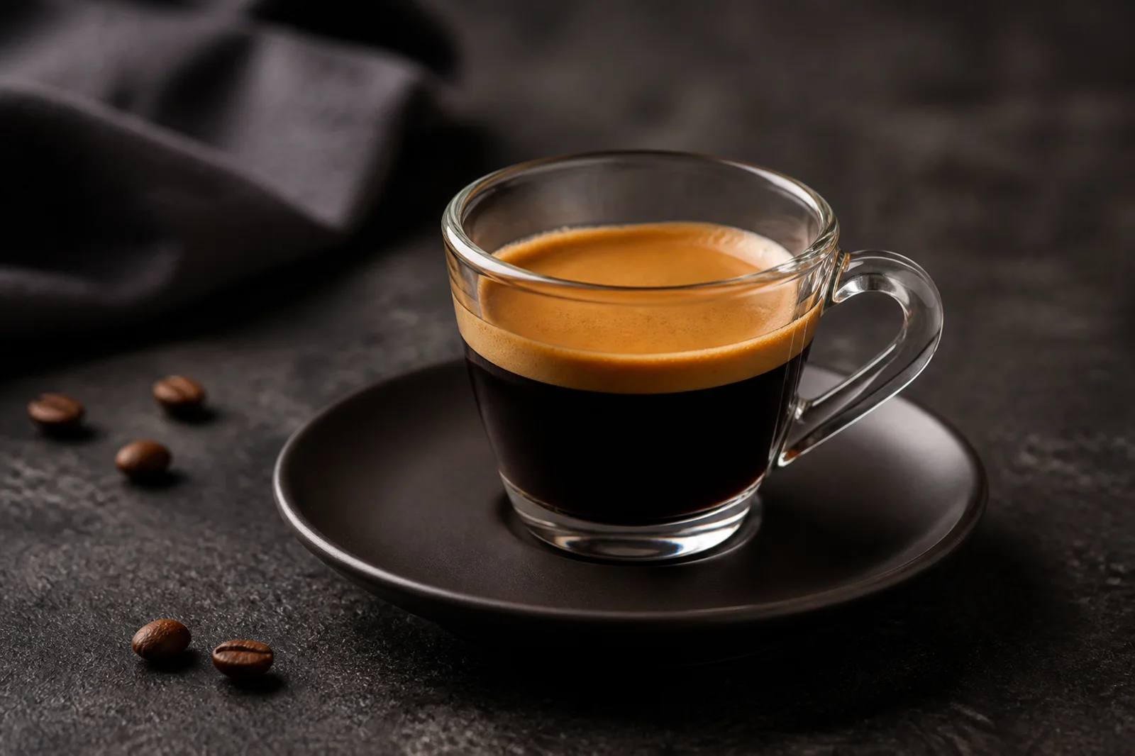 A generic glass espresso cup on a dark table with scattered coffee beans